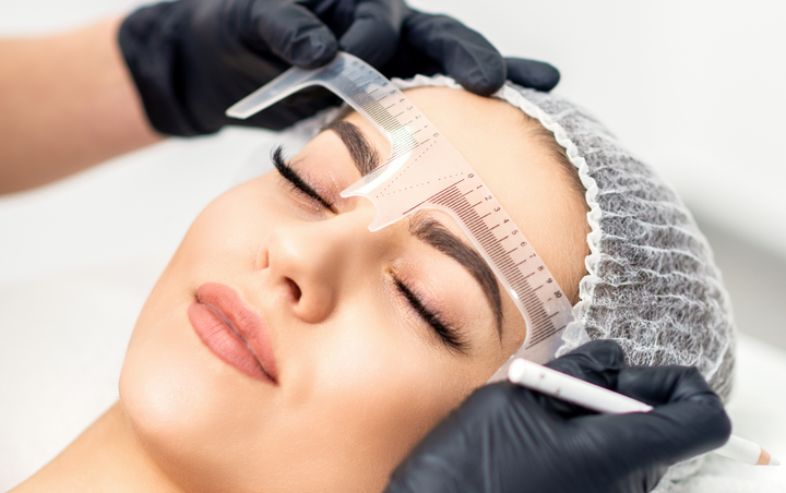 An eyebrow technician measuring a client’s brows